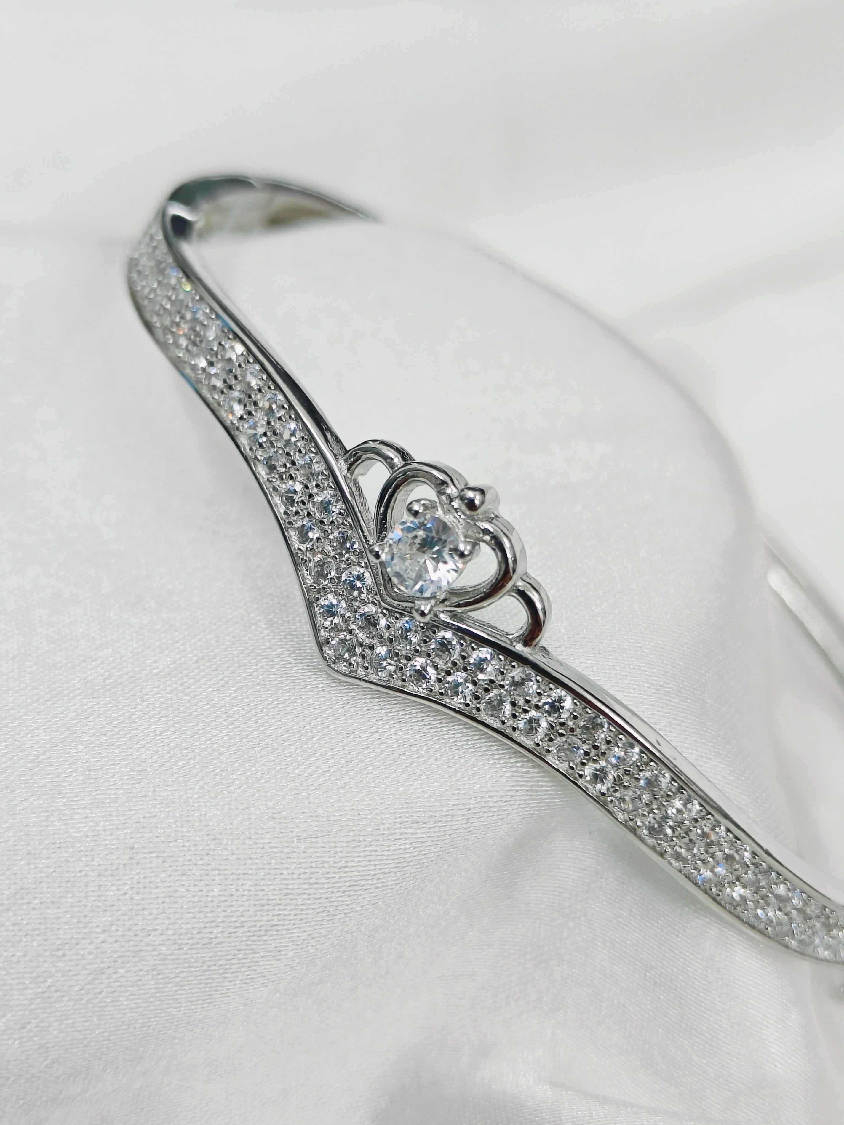 Silver bracelet with heart-shaped clasp and clear stones on a white background